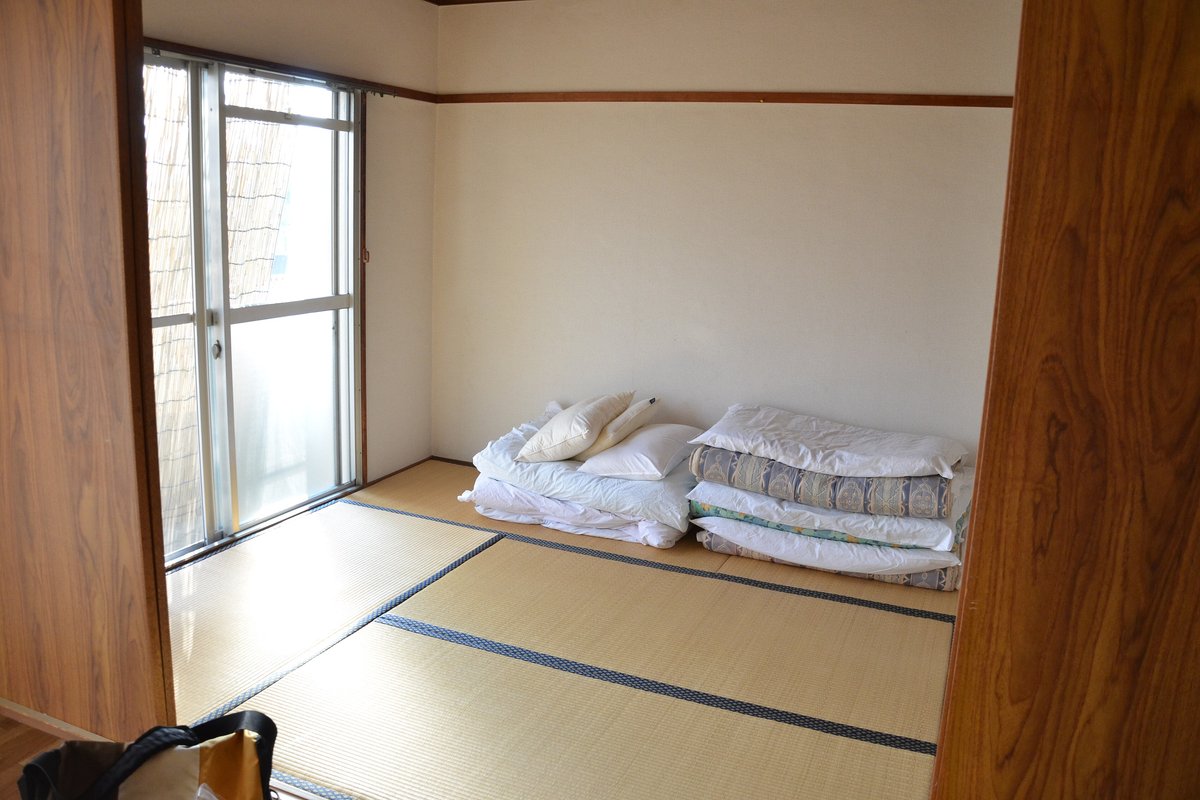 日の差し込む窓際の和室。たたんだ布団と枕が畳の上に置かれている
