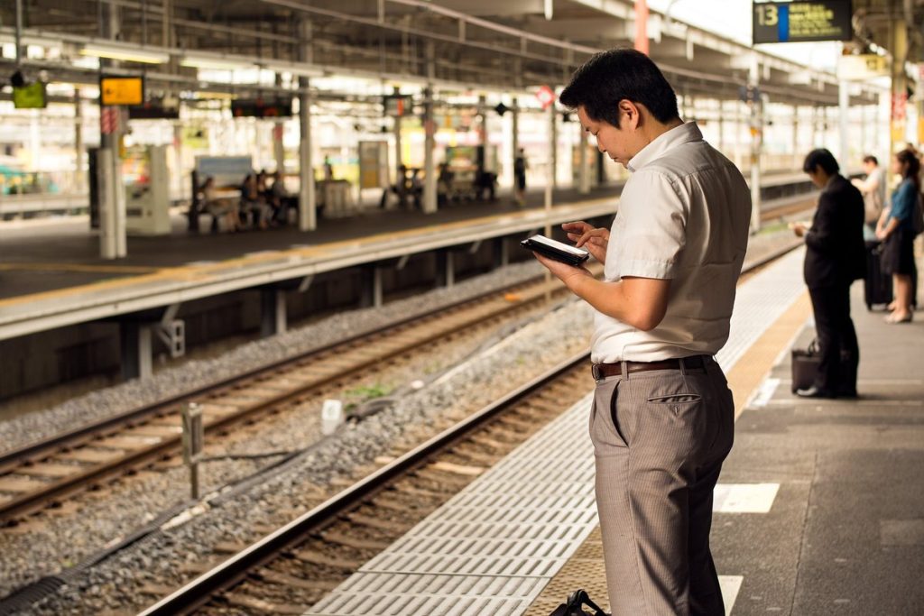 夜の駅のホームで、スマートフォンを見ながら電車を待つ会社員