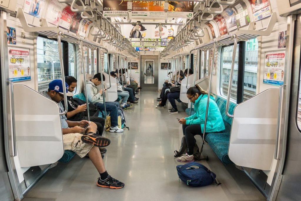 東京の地下鉄の車内で、座ってスマートフォンを見る乗客たち