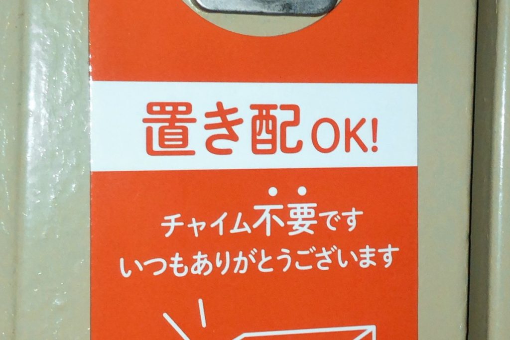 玄関ドアのノブに掛けられた「置き配OK チャイム不要です」と書かれたオレンジ色の札