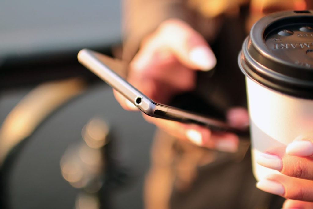 コーヒーカップを持ちながらスマートフォンを操作する手