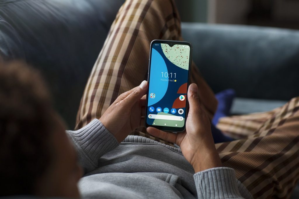 ソファでくつろぎながら両手でスマートフォンを持つ人の手元