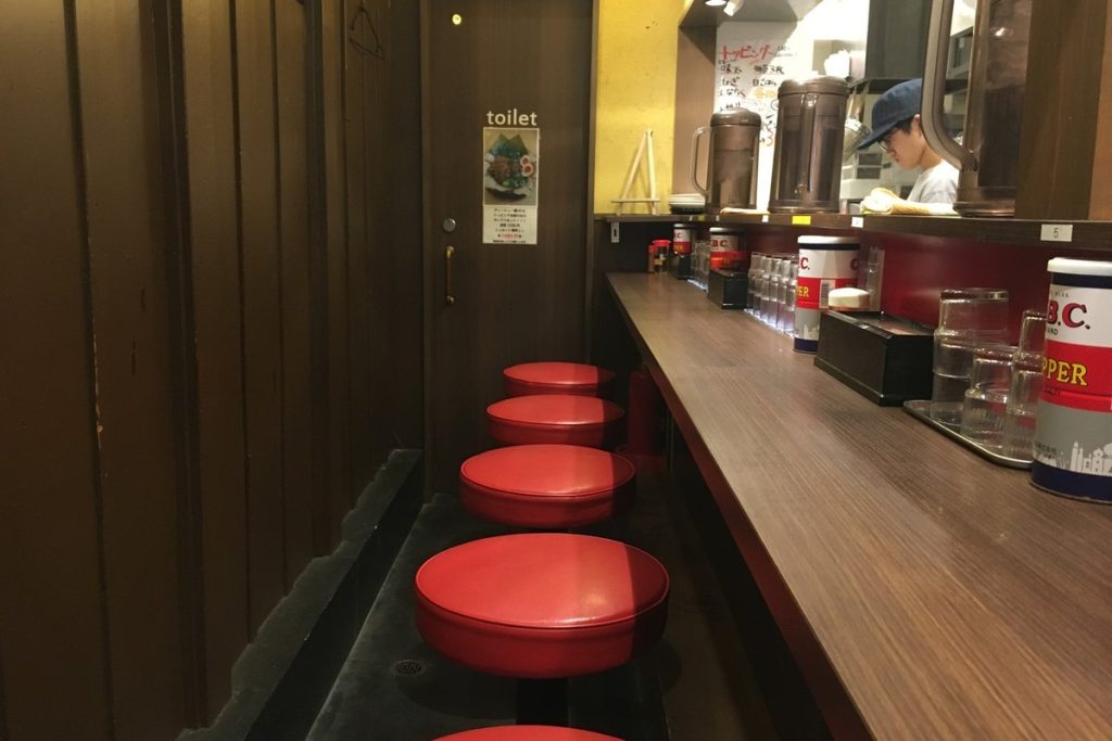 赤い丸椅子が並ぶラーメン店のカウンター