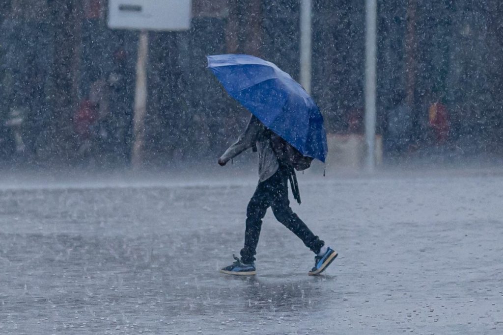 強い雨の中、傘をさして歩く人