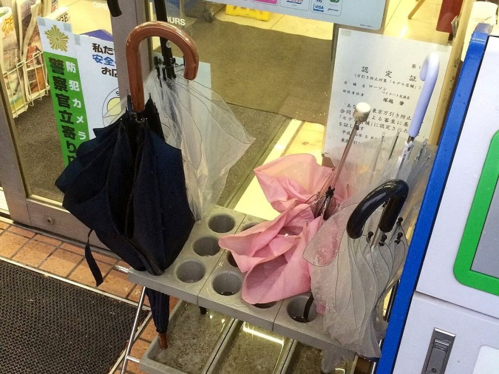 コンビニの入口に置かれた傘立てに、黒い傘やピンクの傘、ビニール傘が差してある様子